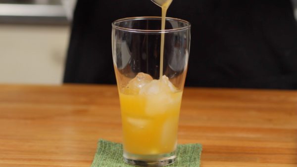 取っておいたメロン果汁を使ってメロンクリームソーダを作ります。グラスに氷とメロン果汁を入れます。シロップを加えて混ぜます。