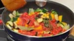 Ajoutez les tomates concassées en boite. Ajoutez une feuille de laurier et des feuilles de thym fraîches. Pressez doucement les tomates concassées dans les légumes. 
