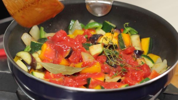 Thêm cà chua thái hạt lựu đóng hộp. Cho lá nguyệt quế và lá xạ hương (thyme) tươi vào. Nhấn nhẹ cà chua thái hạt lựu vào rau củ.
