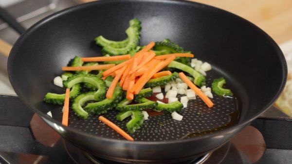 Faites chauffer l'huile d'olive dans une poêle. Ajoutez l'ail hachée, le melon amer et les carottes. Faites revenir les légumes sur feu moyen. 