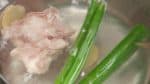 En la misma olla con agua hirviendo, pon la parte verde de una cebolla verde y las rodajas de raíz de jenjibre. Añade el sake. Por último, añade las lonchas finas de cerdo y remuévelas con unos palillos.
