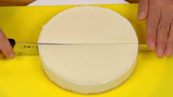 Place the cheesecake onto a cake turntable and remove the bottom of the pan. Wipe the blade of a cake knife with a dampened towel and cut the cake in half. 