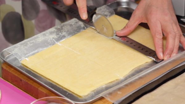 Coat the pastry cutter with flour and divide the sheet into rectangular pieces. Like shown, mark the grid pattern on the sheet so that you can easily cut it into equal pieces. Trim off the edges of the dough.