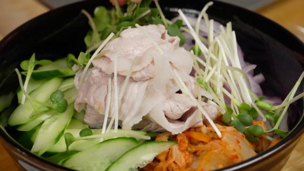 Arrange the toppings onto the soba noodles. Add the kimchi, fermented Korean side dish, red onion, cucumber and pork slices. Finally, distribute the kaiware radish sprouts on top.