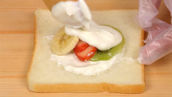 Finally, let’s make the mixed fruit sandwich. Place the kiwi fruit, strawberry and banana slices onto the cream layer. Spread more yogurt cream onto the fruits.