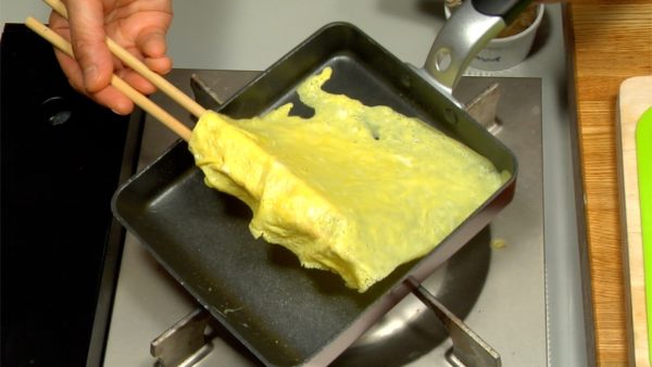 When the egg is almost cooked, turn off the burner. Flip the omelette with chopsticks, cook the other side, and place it on a cutting board.