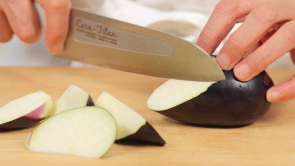 Trim off the stem end of the eggplant. Cut the eggplant into bite-size wedges by turning it after each cut as Chef is doing here.