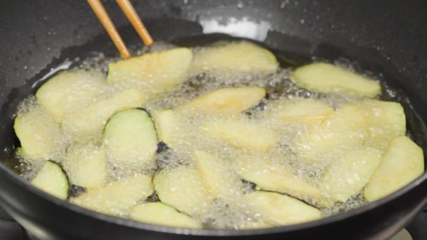 Heat the frying oil to 180°C (360°F) in a pot. Place the eggplant into the oil with the skin side facing down. This will help to give the skin an appetizing purple color, making it visually appealing.