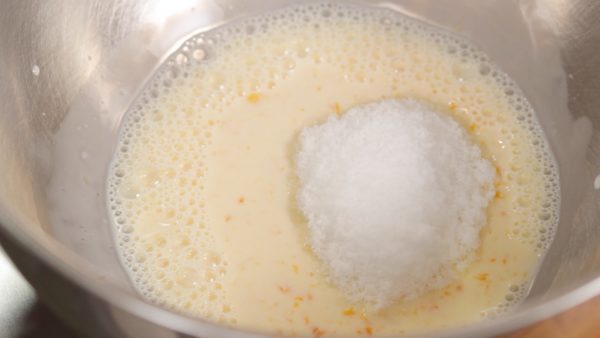 让我们先做面糊。把牛奶加入蛋黄搅里拌混合。然后，加入糖直到完全溶解。
