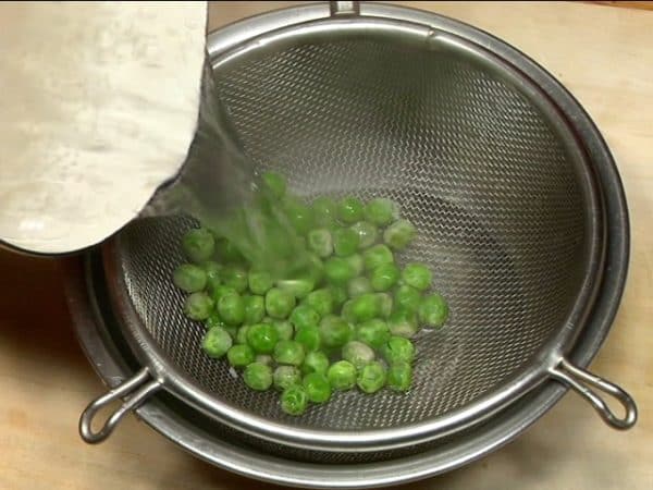 Place the frozen green peas into a mesh strainer. Briefly rinse under hot water, removing the freezer smells. Strain and salt the peas.