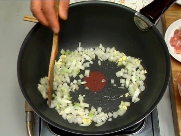 Vamos fazer o arroz com frango. Coloque azeite de oliva em uma frigideira. Refogue o alho em fogo baixo. Quando o aroma ficar mais forte, adicione a cebola e refogue em fogo médio.
