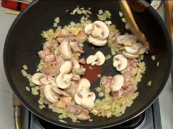 When the chicken begins to brown, add the button mushrooms. Continue to stir and distribute the oil evenly. Add the white wine and allow the alcohol to evaporate completely.