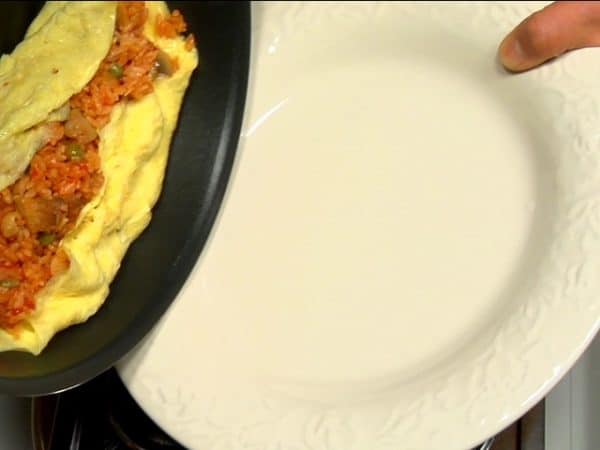 Retourner l'omurice sur une assiette. Les oeufs continuent de cuire tant qu'ils sont au chaud alors il faut le faire rapidement.