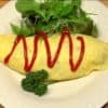 Shape the omurice with a paper towel. Place the baby salad greens and parsley leaves next to the omurice. Finally, garnish with the tomato ketchup.