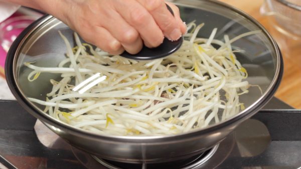 Rincez les germes de soja et retirez les deux bouts. Placez-les dans la poêle. Ajoutez une pincée de sel et l'huile de sésame. Couvrez et allumez le feu. Faites chauffer la poêle pendant 2 minutes. 