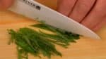 Chúng tôi sẽ cắt các nguyên liệu cho Ochazuke. Cắt những chiếc lá tía tô làm đôi theo chiều dọc. Chồng lá lên nhau và thái thành các dải vừa bằng những đường cắt chéo. Cắt rau mùi tây Nhật Bản (mitsuba parsley) thành dài khoảng 3 inch. Xếp chúng lại và thái thành các miếng vừa.
