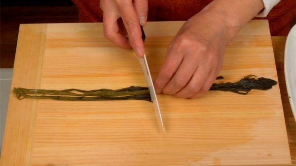 Cut the takana-zuke, pickled takana greens, into manageable pieces as well; line them up and chop finely.