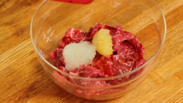 Let's make the taco meat. These are beef slices for yakiniku, cut into bite-size pieces. Add the soy sauce, grated garlic clove, grated onion and tomato ketchup. Gently distribute the seasoning.