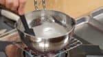 Vamos fazer o xarope. Combine a água e o açúcar numa panela. Ligue o forno e dissolva o açúcar. Quando começar a ferver, diminua o fogo. Reduza o xarope por 2 a 3 minutos.