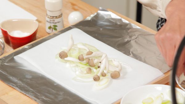 Place a sheet of parchment paper onto a larger piece of aluminum foil. Arrange 2/3 of the long green onions along with 2/3 of the shimeji and maitake mushrooms onto the paper.