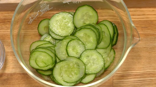 Let's cut the vegetables. Slice the cucumber into thin slices. Sprinkle on the salt and toss to coat in a bowl. Let it sit until slightly softened and then squeeze out the excess water.