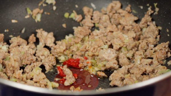 Reduce the heat to low. Make a space in the center of the pan. Add a small amount of vegetable oil and doubanjiang, chili bean paste to the space. Stir-fry the doubanjiang and bring out the aroma and pungent flavor.