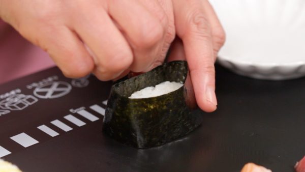 Next, make the Gunkanmaki for the salmon roe also known as ikura. Wrap the side of the rice with the nori strip. With a rice grain, close the end of the nori.