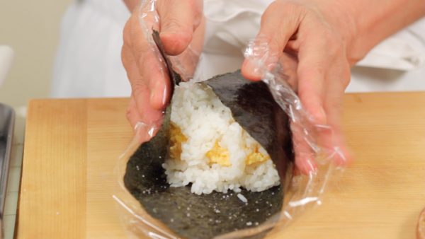 Fold the left and right corners of the nori seaweed along with the plastic wrap.