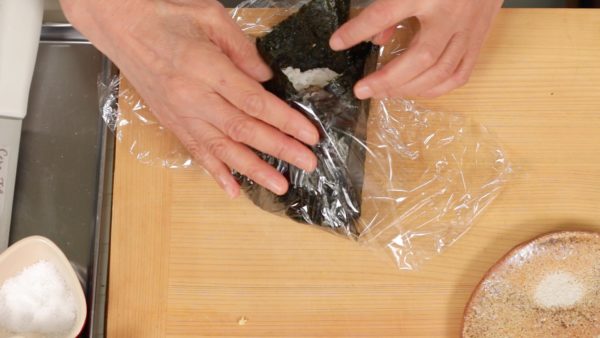Then, fold the top and bottom corners. Wrap it with the plastic wrap and let the onigirazu sit with the folded side facing down.