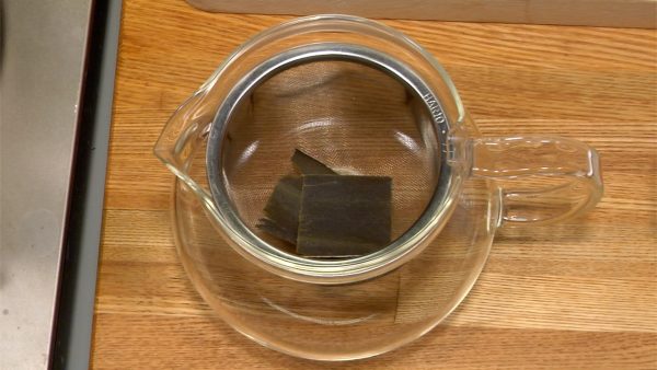Prepariamo il brodo dashi. Togliere i residui di polvere e sabbia dall'alga Kombu. Mettere i pezzi di Kombu in una tazza da tè con colino incorporato. 