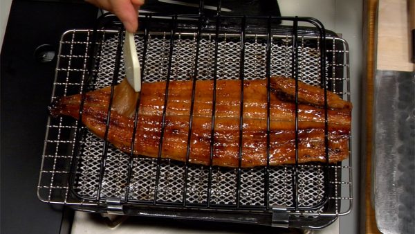 Taut den Unagi vorab auf und erhitzt ihn nun über dem Gaskocher in einem Fischrost. Röstet ihn zuerst auf der Hautseite. Bestreicht die Fleischseite mit Sake, um den Unagi zart zu machen. Geht sicher, dass ihr den Unagi gleichmäßig röstet. 