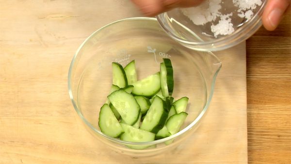 Let's prepare the ingredients for Bento. Cut the cucumber vertically in half. Slice the cucumber into half moons. Put the cucumber in a bowl, add a pinch of salt, and toss to coat evenly.