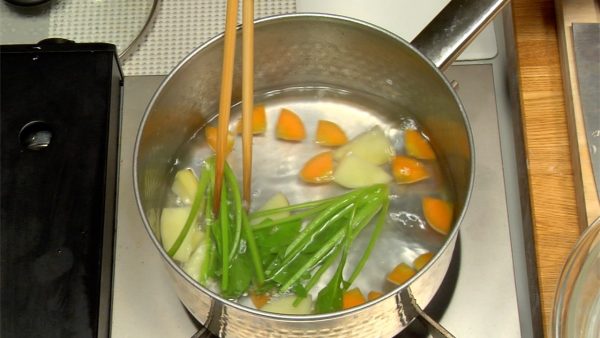 Let's cook the vegetables. Prepare a pot of water with added salt. Put in the potato and carrot, cover, and turn on the burner. When the water boils, cook the stem part of the spinach first.