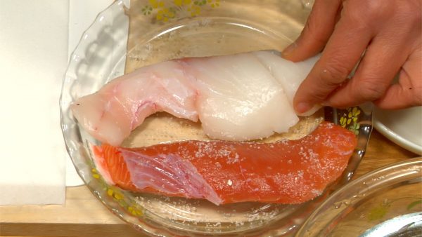 Let's prepare the salmon and pacific cod. Sprinkle salt on both sides of the fillets. Lightly press the salt into the fillets with your hands. Let it sit for 20 minutes until the surface becomes slightly wet.
