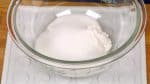 Vamos a preparar el mochi, arroz pegajoso aporreado. Combina la harina de arroz pegajosa con azúcar en un bol apto para microondas y mézclalo bien con una espátula.