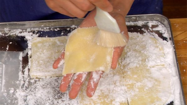 With a scraper, place each mochi onto your palm. Remove the excess starch with a pastry brush. Flip it over and remove the starch on the other side.