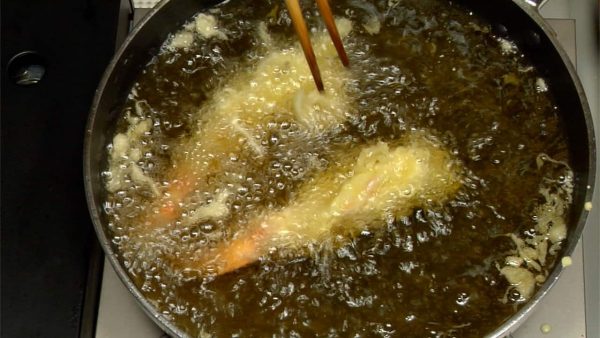Plongez une autre crevette dans la pâte et faites-la frire avec la première. Attachez des petits morceaux de pâte à tempura à la crevette à nouveau. 