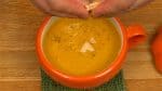 把南瓜湯舀進碗裡。用廚房布擦去任何點滴，然後將碗放在杯墊上。撒上胡椒粉。最後，在上面放上碎餅乾。
