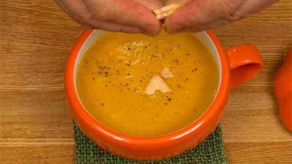 把南瓜汤舀进碗里。 用厨房布擦去任何点滴，然后将碗放在杯垫上。 撒上胡椒粉。 最后，在上面放上碎饼干。