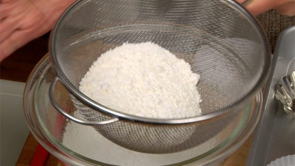 Mari membuat adonan untuk mushipan. Campur tepung kue (terigu protein rendah), baking powder, dan sejumput garam dalam saringan lalu ayak semuanya ke dalam mangkuk.