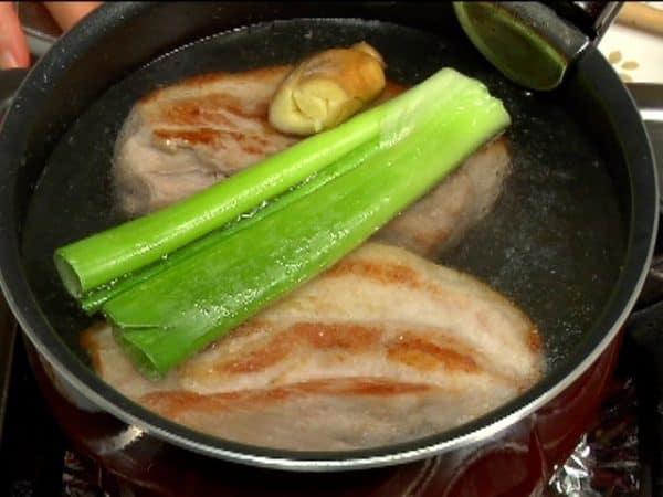 Aggiungere acqua nella pentola fino a coprire la pancetta. Aggiungere la parte verde del cipollotto e lo zenzero schiacciato.