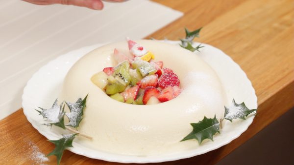Place the fruit mixture into the center of the ring. Garnish with the holly leaves and the Christmas ornament. Finally, sprinkle on the icing sugar.