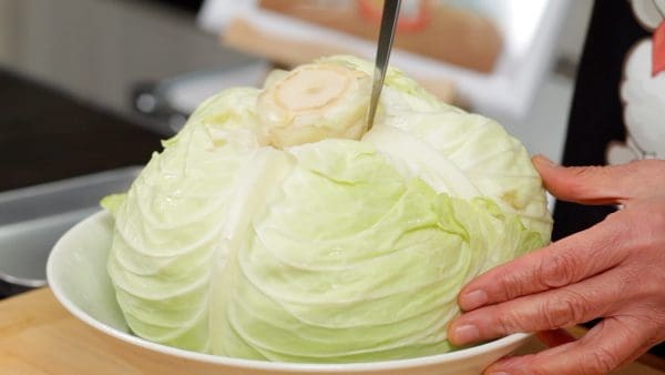 Let's cook the cabbage. Insert the blade of the knife along the core, and remove it from the cabbage. Removing the core at this stage makes it easy to separate each leaf later.