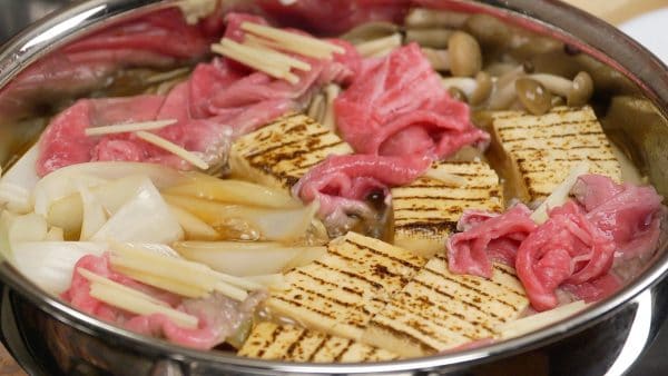 Then, distribute the thin beef slices among the ingredients. Add the shredded ginger root. Submerge the beef slices into the broth to cook evenly.