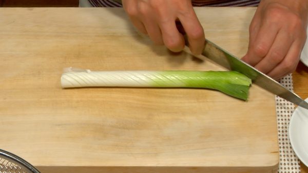 Let's chop the spring onion. Make equally spaced diagonal cuts in the spring onion. Flip it over and repeat the cuts in the other side.