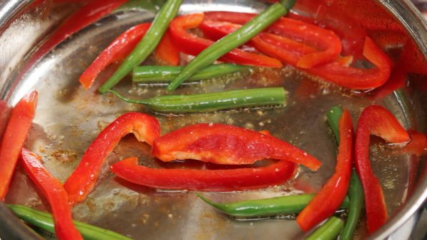 Next, add 1cm (0.4") thick red bell pepper strips and half-cut string bean pods. Season them with salt and pepper. Stir-fry the vegetables.
