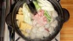 Add the aburaage, thin deep-fried tofu, cabbage leaves, long green onion, the stalk part of the garlic chives, and the extra-thin pork slices. We are using the pork slices for shabu-shabu, a Japanese hot pot dish.