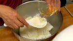 戴上廚房用一次性手套，把米飯放在碗裡，將剩下的壽司醋倒入碗中，和米飯攪拌均勻。