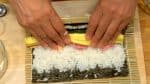 小心地把竹簾的邊緣抬起，開始卷太卷壽司，卷的時候也要注意握著配料，不要讓它鬆散開。