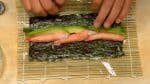 把黃瓜放在海苔的中間。然後把牛油果和蟹棒並排放好。抬起竹簾的邊緣滾動，按住配料，不要讓它鬆散開。